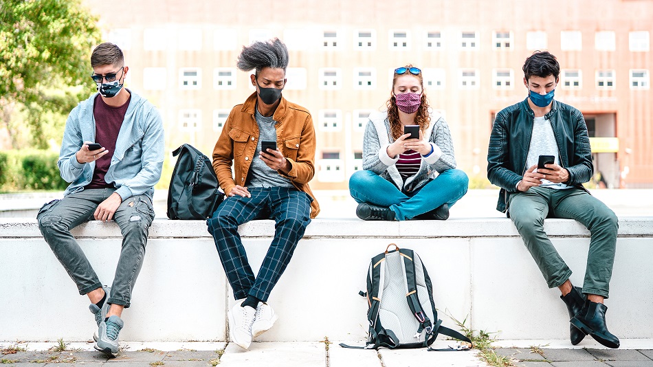 Millenial friends using smart phones with face mask on Covid sec