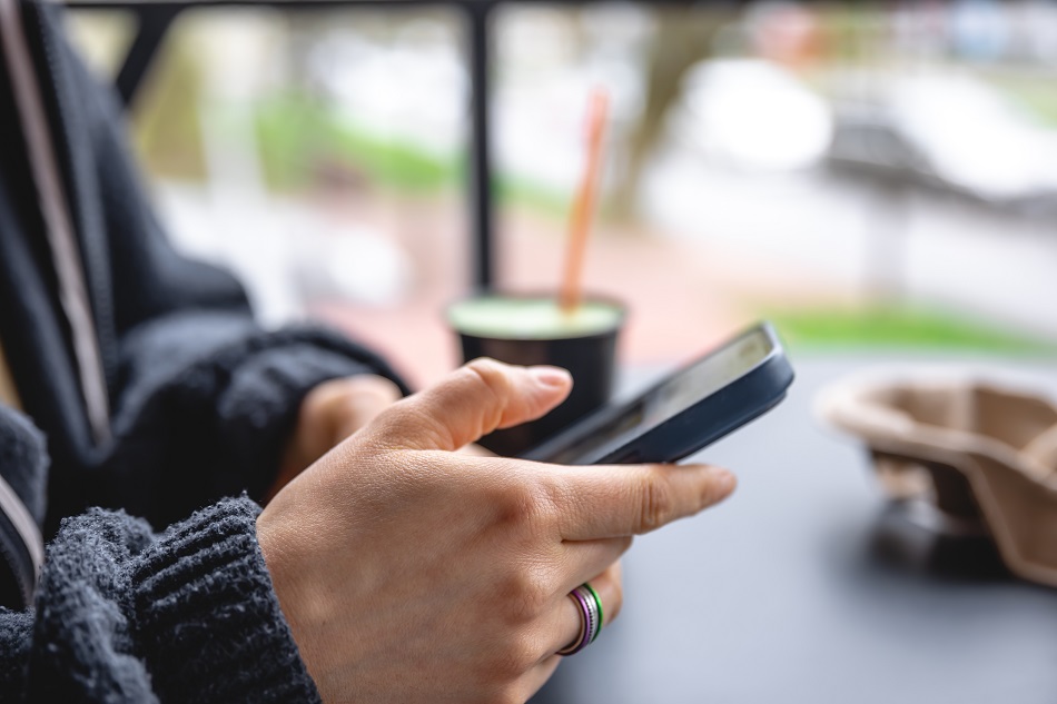A woman sits on the terrace of a cafe and uses a smartphone, close-up.