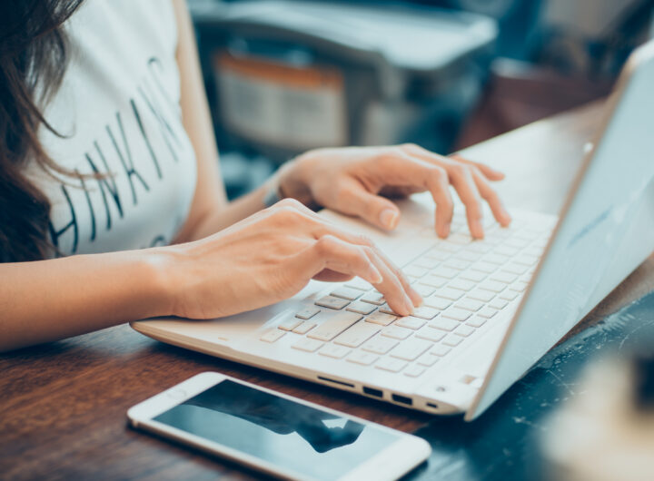 beautiful young hipster woman's hands busy working on her laptop sitting at wooden table in a coffee shop