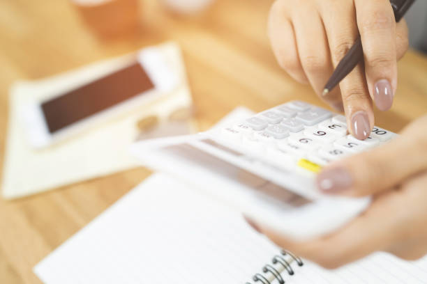 close up hand view of business man using calculator on her and mobile smart phone press button keyboard used for mathematical calculations. documents on table. concept calculate account finance